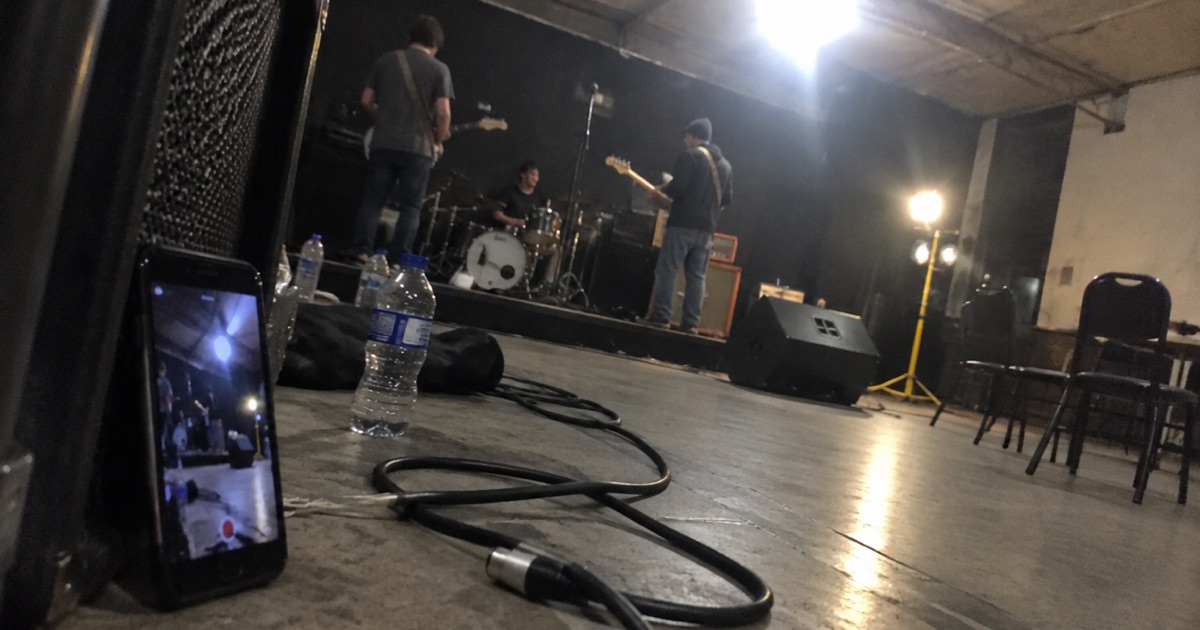 Phone snapshot of a phone propped crookedly against an amp at the side of a stage, filming a soundcheck.