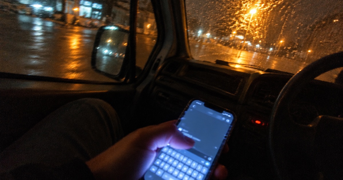 Phone snapshot inside a parked van at night, a phone screen glowing on someone's fingers mid-typing.