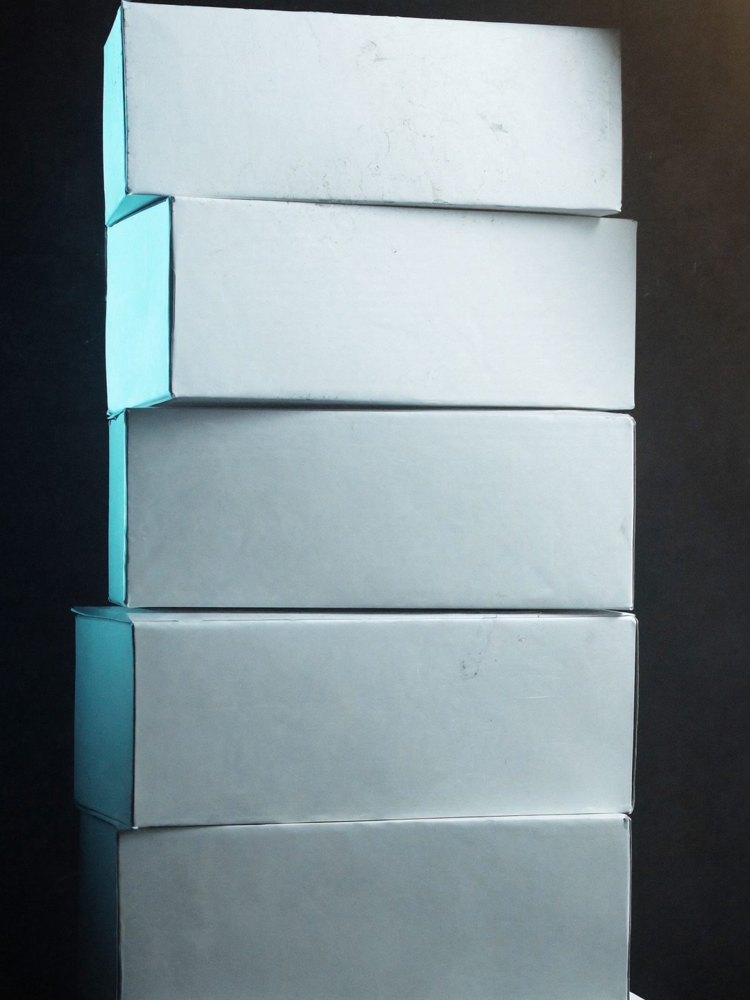 Unmarked archival document boxes stacked on a dark table under raking light