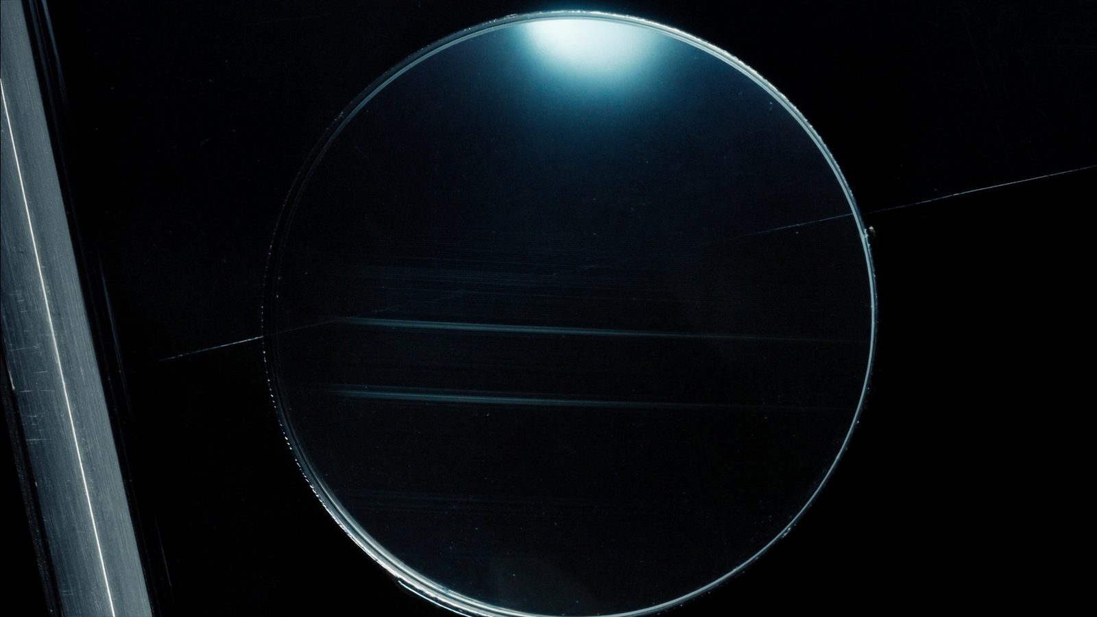 Magnifying lens over a dark screen surface catching a cyan highlight